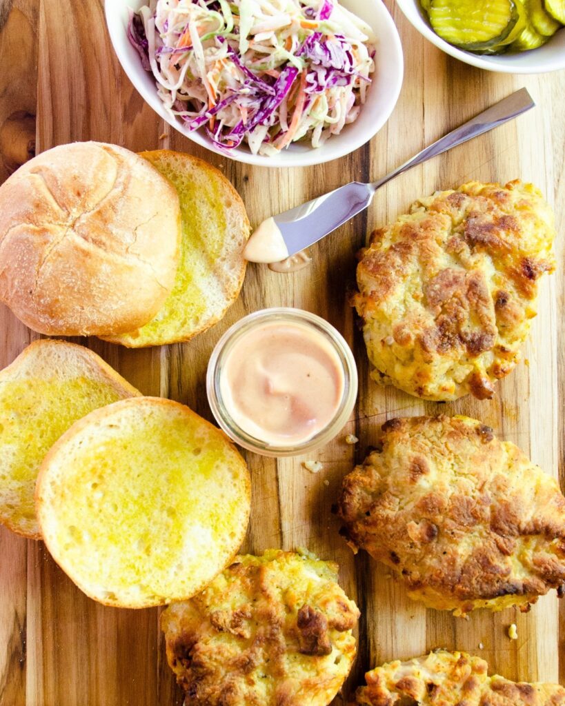 The makings of an air-fried chicken sandwich on a wooden board - coleslaw, special sauce, buns and fried chicken.