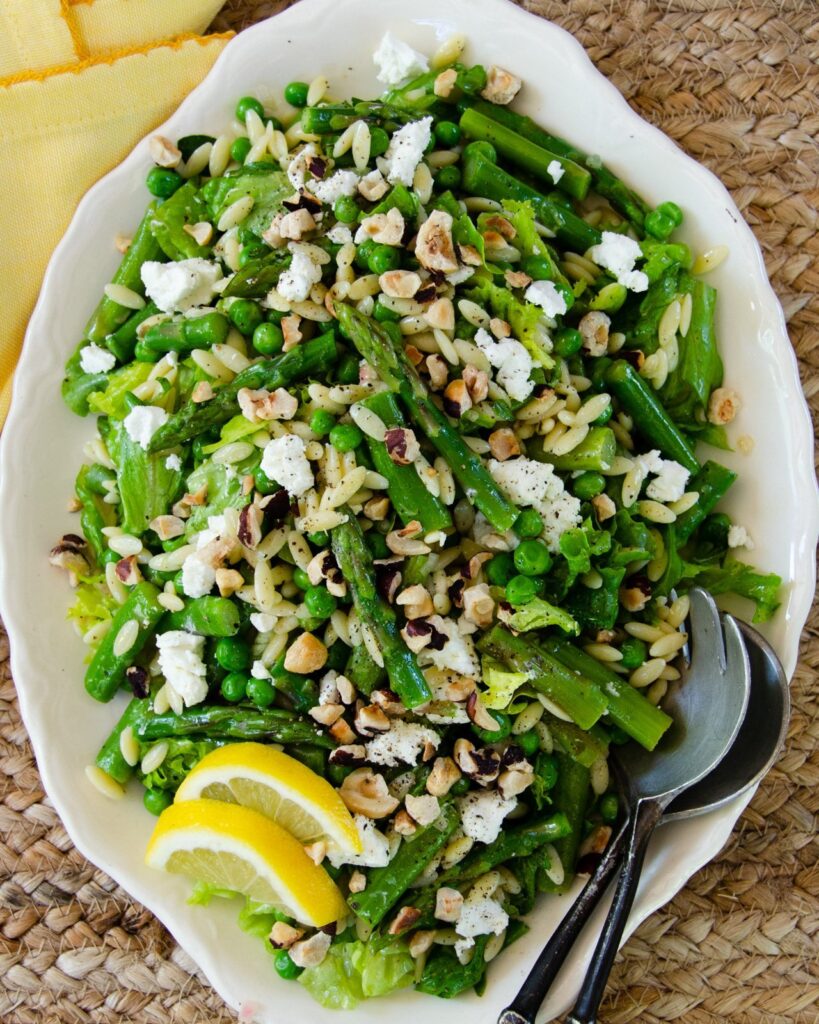 Spring green salad on a white oval platter with serving spoons.