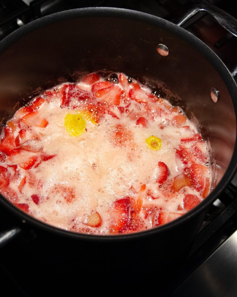 Strawberries and rhubarb simmering in a pot with lemon halves.
