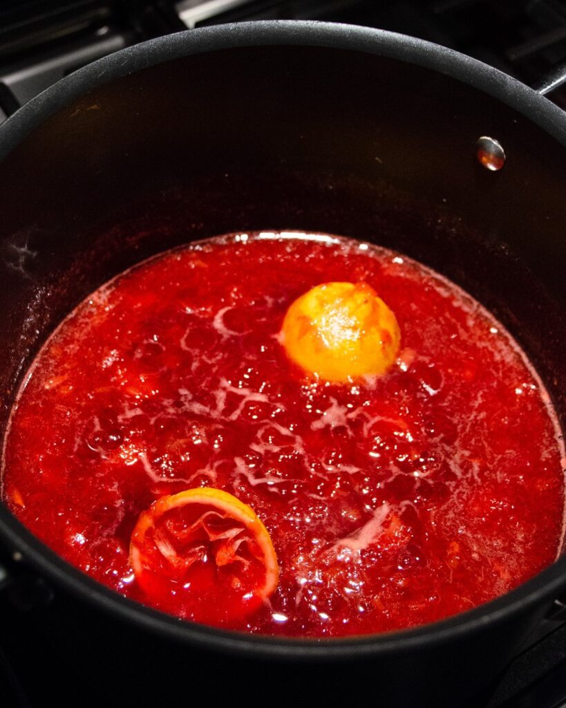 Strawberry Rhubarb Jam simmering in a pot with lemon halves.