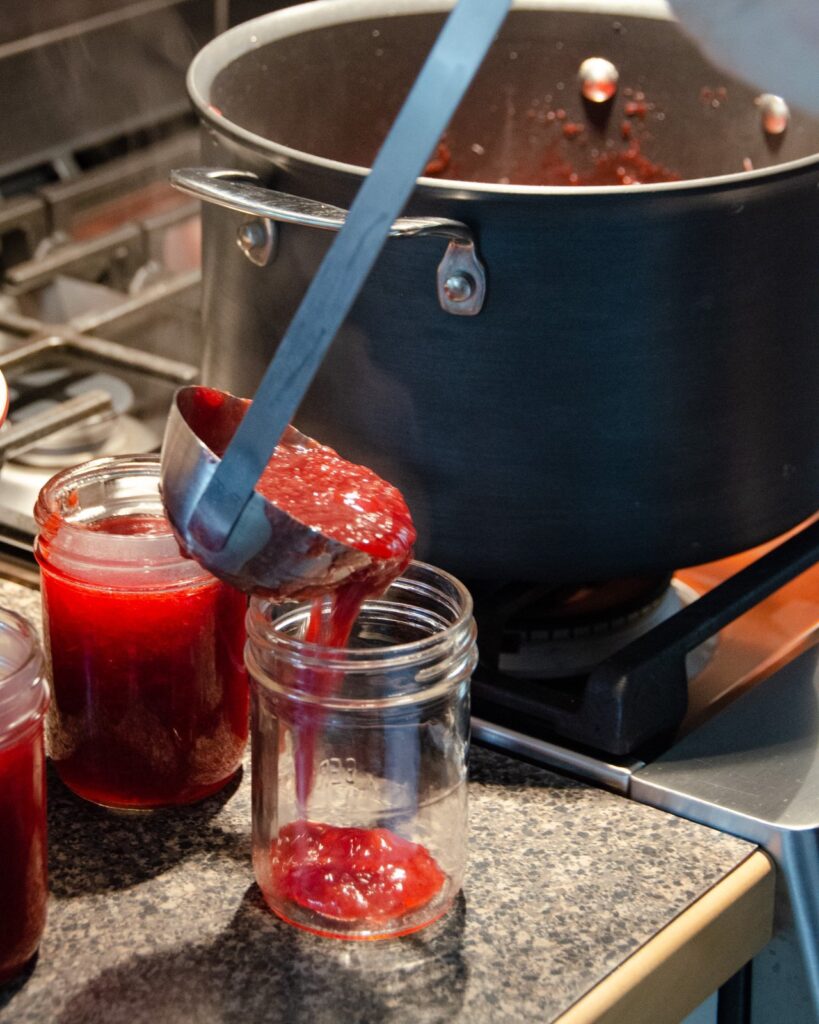 Transferring strawberry rhubarb jam into jars with a ladle.