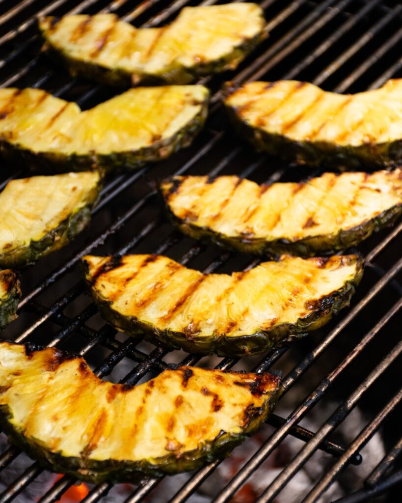 Glazed grilled pineapple Pineapple slices on a charcoal grill grate.