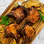 Grilled brined pork chops on a wooden board with pineapple and parsley.