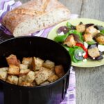 Herbed Sourdough Croutons in an air fryer with a salad and a loaf of bread.