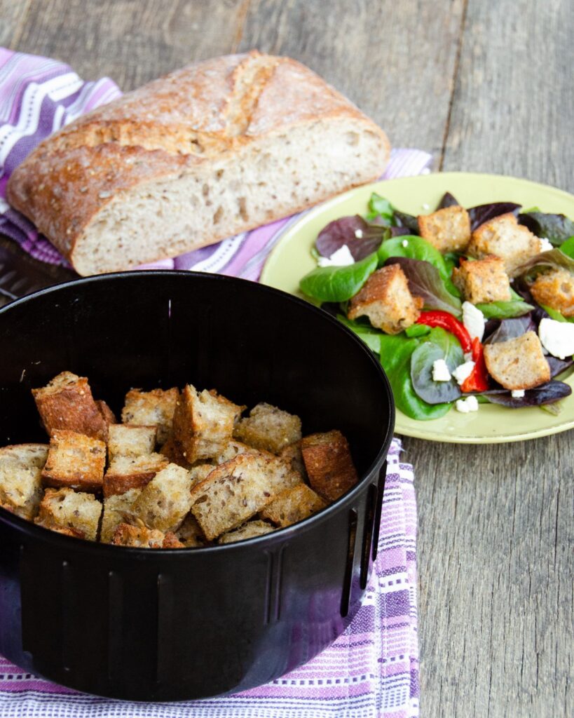 Herbed Sourdough Croutons in an air fryer with a salad and a loaf of bread.