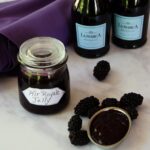 Kir Royale Blackberry Jelly in a jar with prosecco and blackberries on a marble counter.