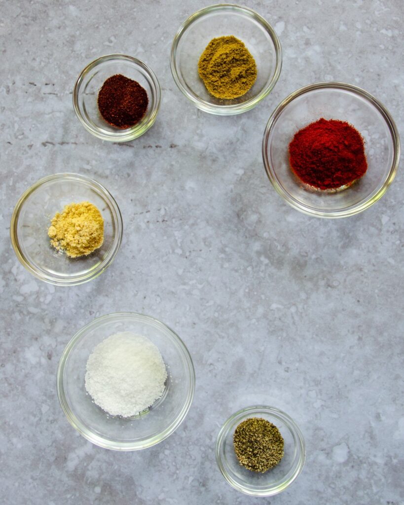 A collection of spices in small glass bowls on a countertop.