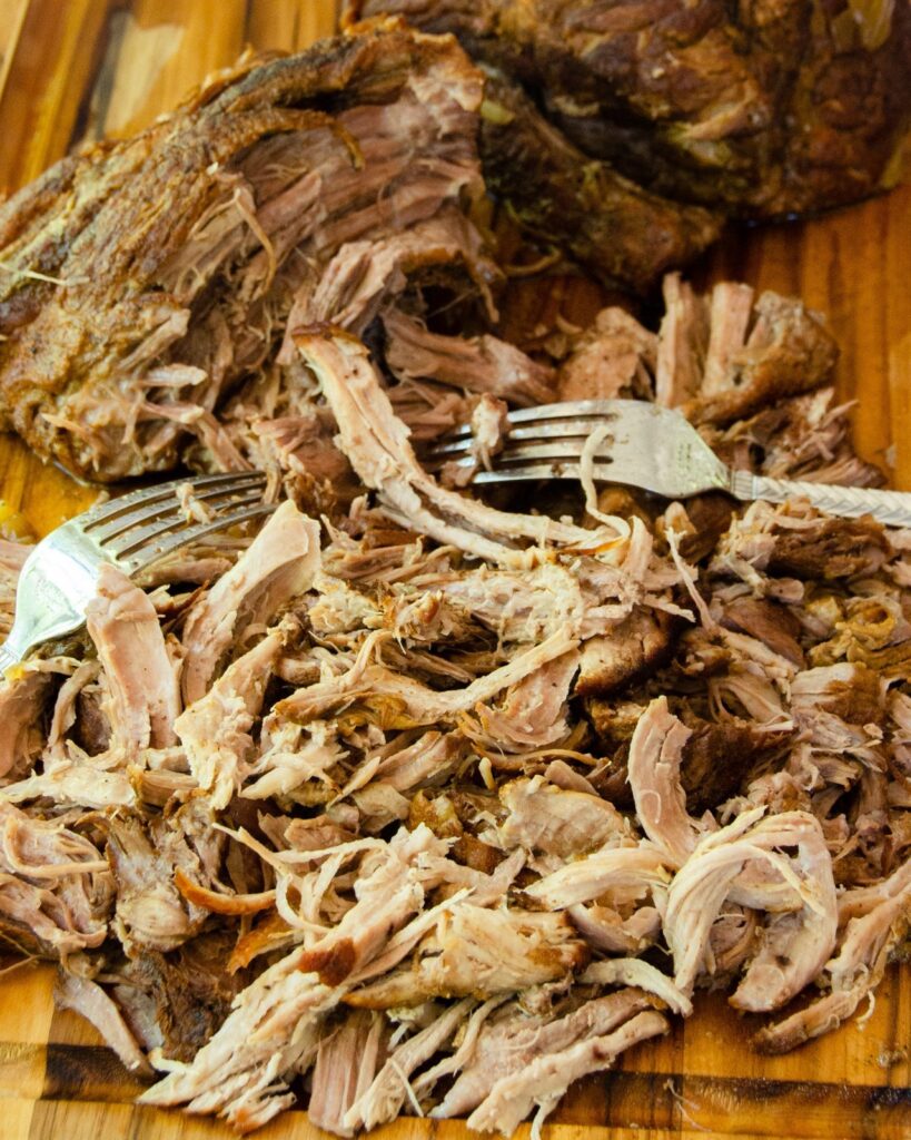 Pork butt being pulled on a wooden cutting board.