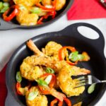 Air-fried salt and pepper shrimp with sliced cherry peppers and scallions in a black dish with red napkins.