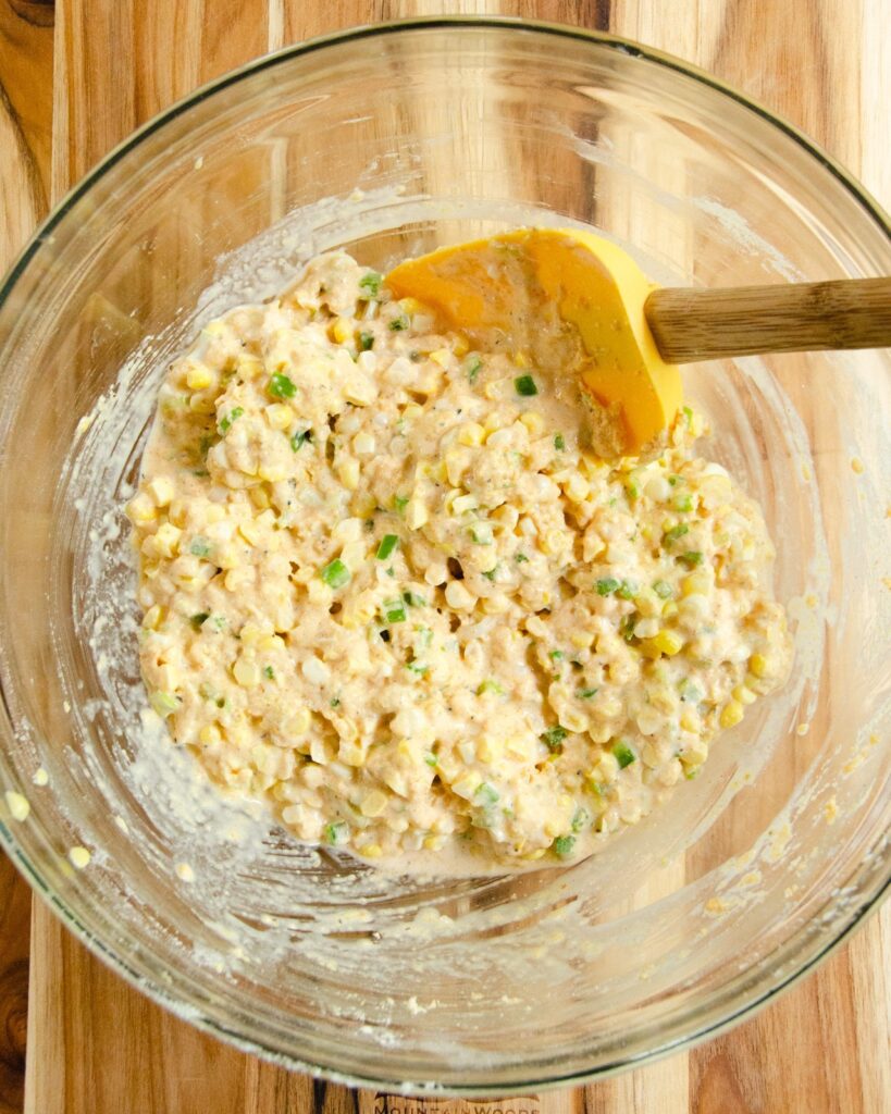 Spicy Corn Cake batter in a glass bowl with a yellow spatula.