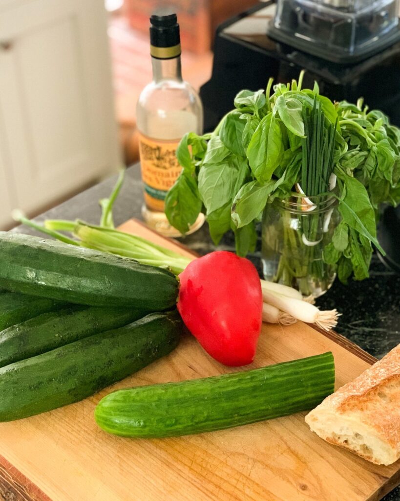 Ingredients for Zucchini Basil Gazpacho on a wooden cutting board with a blender in the background.