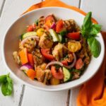 Grilled Panzanella Salad in a white bowl with an orange napkin on a white wooden table.