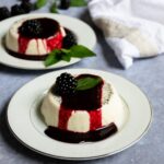 2 white plates with panna cotta and blackberry brandy sauce.