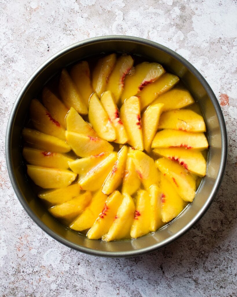 A cake pan on a countertop with slices of peach in the bottom.