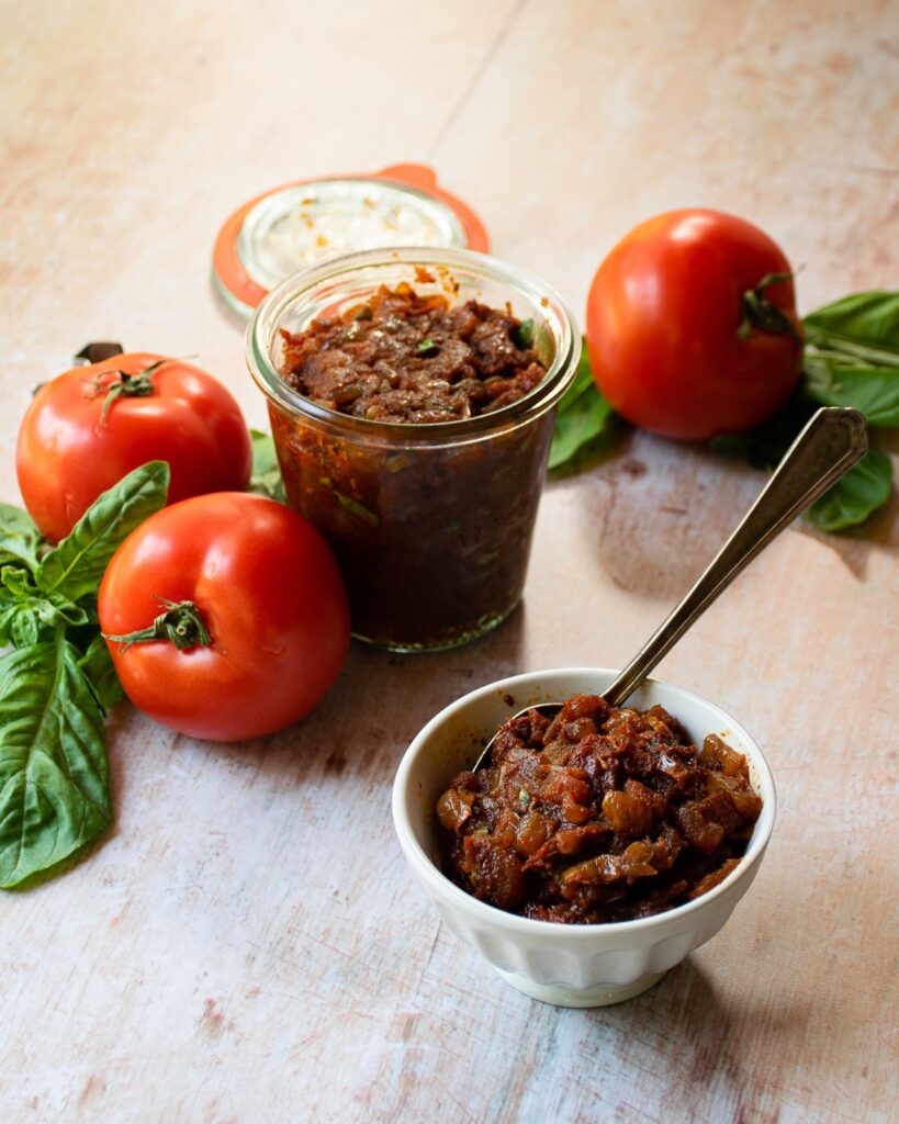 Tomato jam in a little dish with the open jar and a few tomatoes behind it.