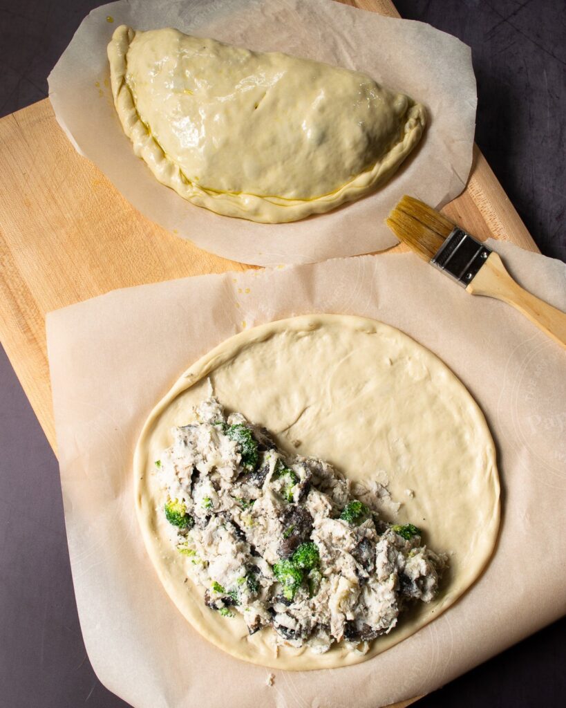 Building a calzone with one completely folded and another partially filled with filling, ready to fold the dough over.