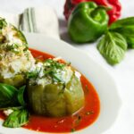 Turkey and Zucchini stuffed peppers on a white plate in a pool of marinara sauce with peppers in the background.