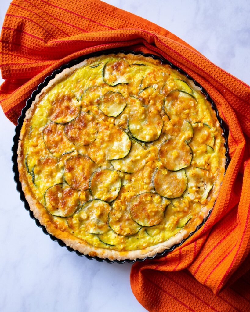 Zucchini and Corn Tart, finished on a counter with an orange towel around half of it.
