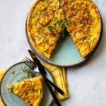 Zucchini and Corn tart on a counter with a yellow napkin and a piece served out onto a plate.