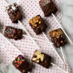 Brownie Pops with various toppings resting on red polka dot paper on a marble counter.