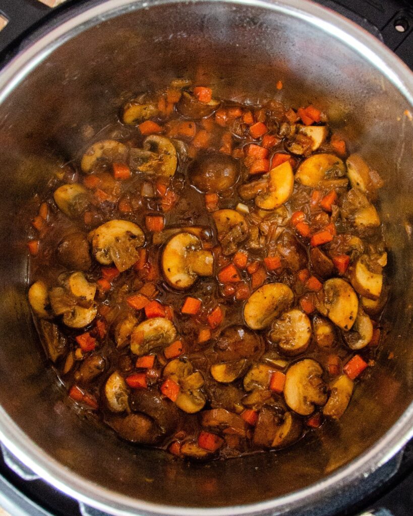 Mushrooms and vegetables in the bottom of an Instant Pot.