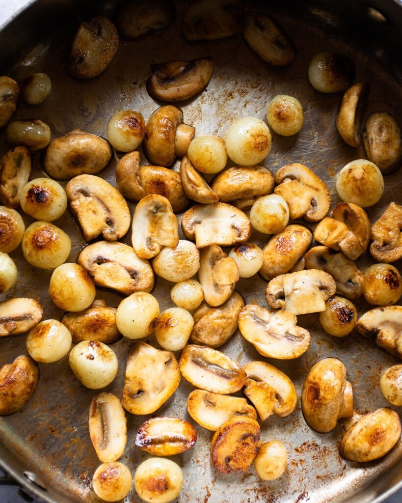Button mushrooms browning in a pan.