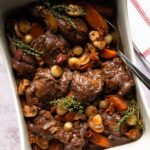 Coq au Vin in a white rectangular casserole with serving spoon.
