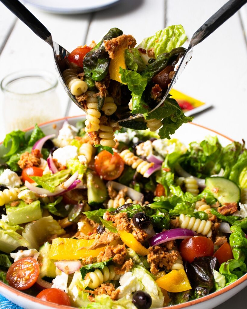 Salad servers serving up a portion of Tuna Greek Salad.