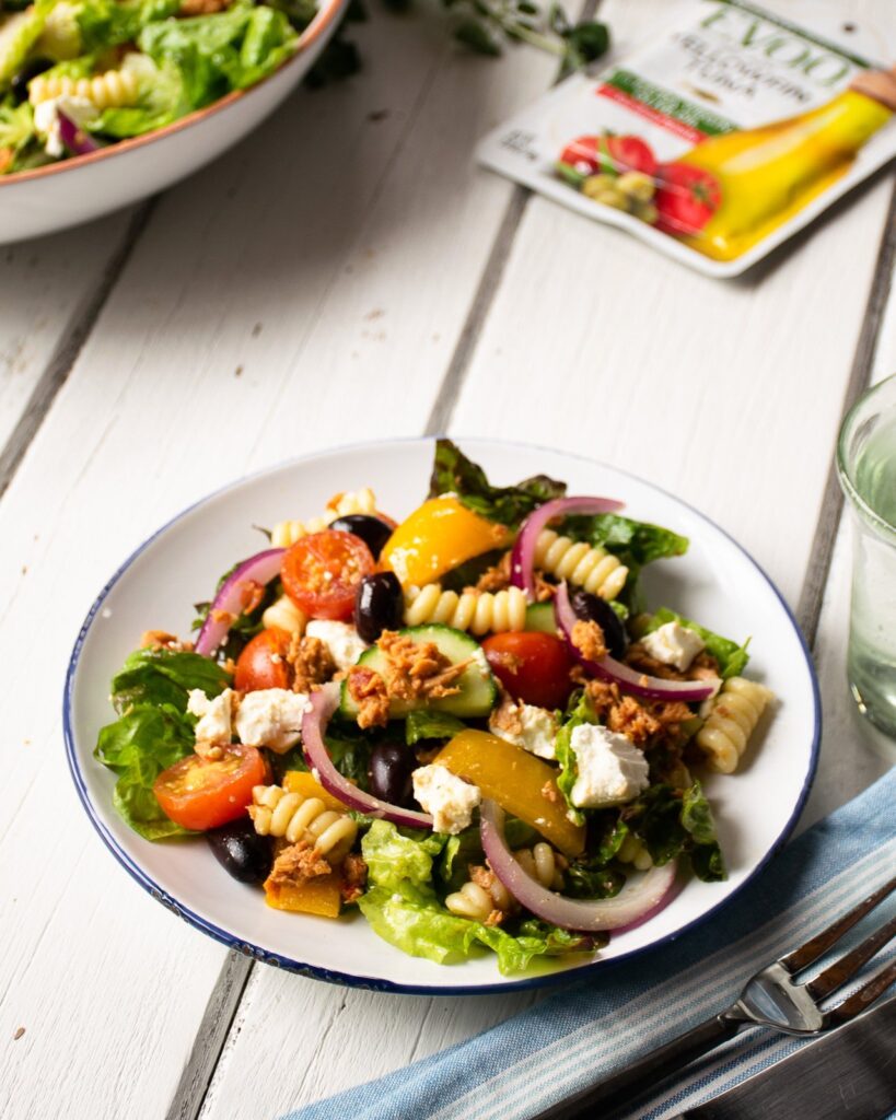 A single serving of tuna greek salad on a white plate with blue rim.