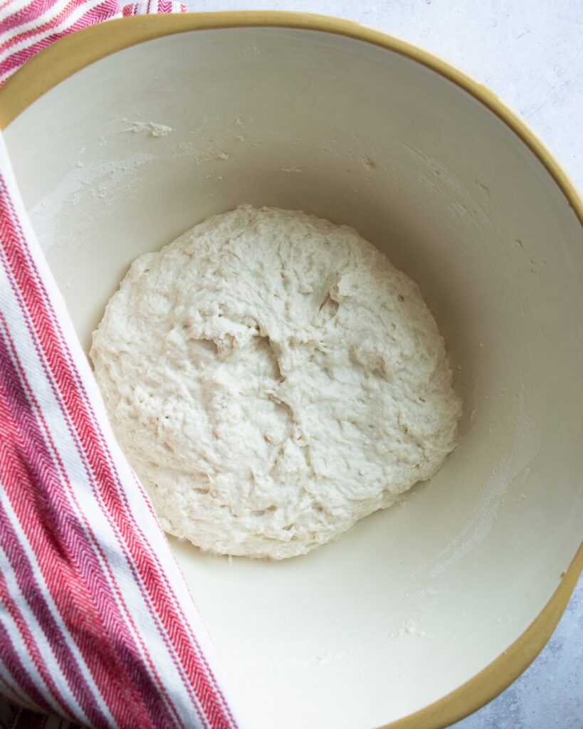 Baguette Dough in a bowl with a red and white striped towel.