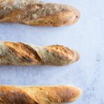 Three homemade French baguettes on a marble surface.
