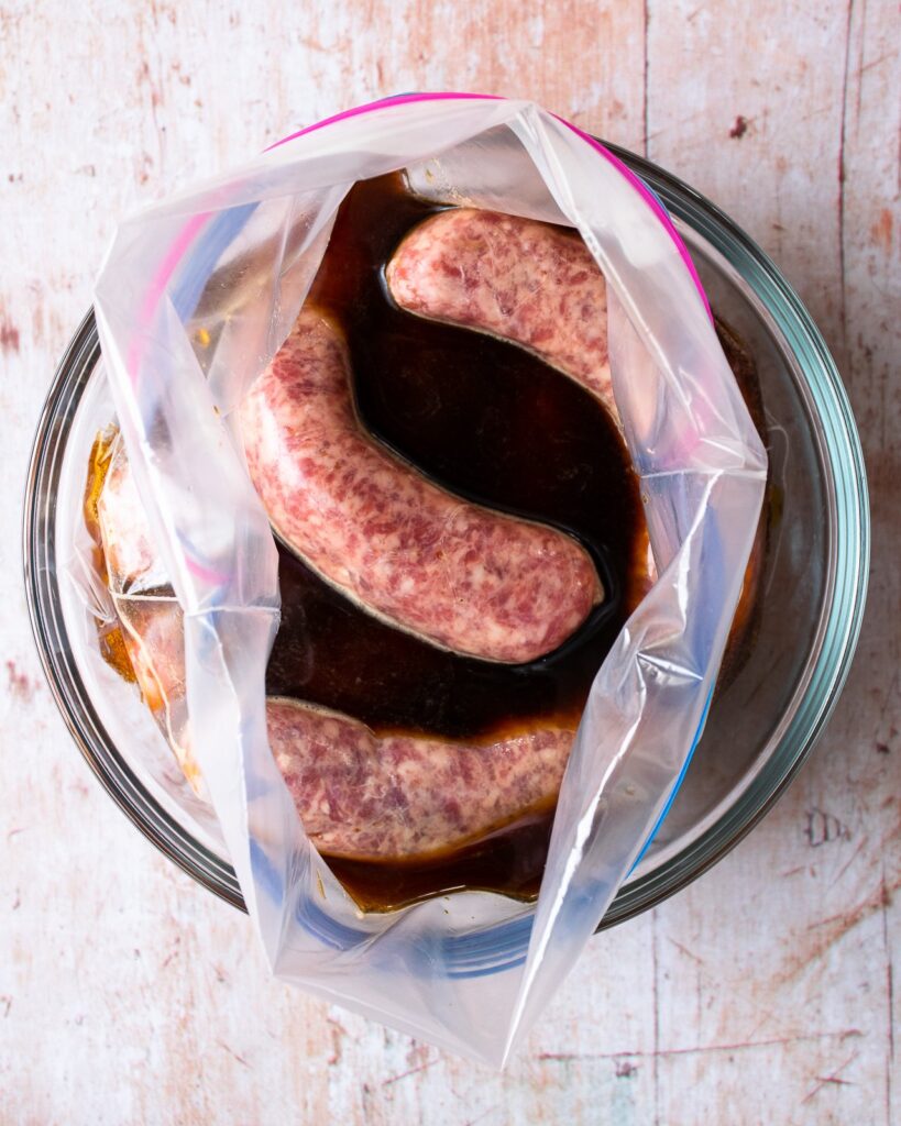 Bratwurst sausages in a bag full of beer marinade, in a bowl on a table.