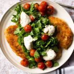 Chicken Paillard with Burrata and Roasted Cherry Tomatoes on a white platter.