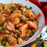 Close up shot of jambalaya in a white bowl with serving utensils and a colorful napkin.