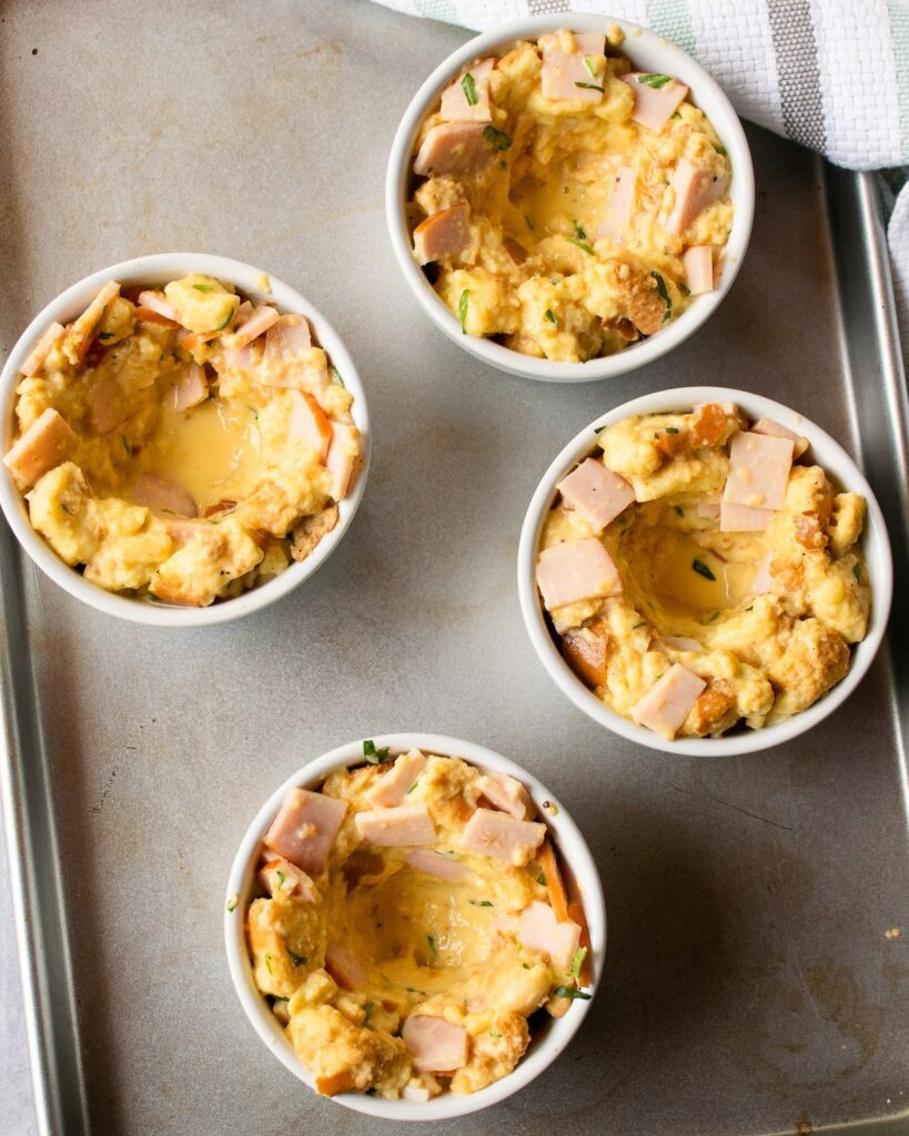 Four ramekins of bread pudding with holes in the center on a baking sheet.