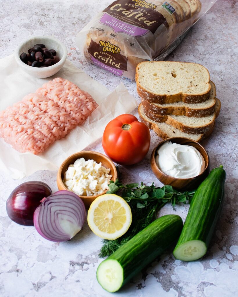 Ingredients for Greek turkey burgers - ground turkey, bread, tomato, yogurt, cucumber, lemon, red onion and olives.
