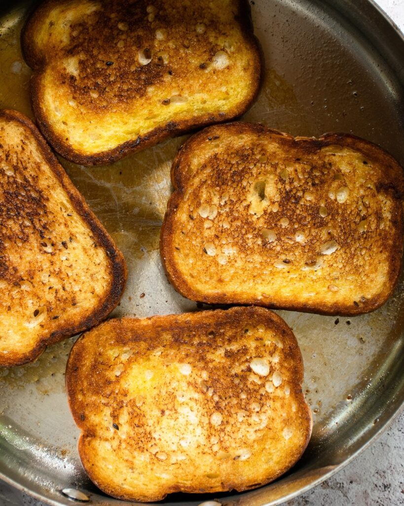 Large pieces of bread frying in a sauté pan.