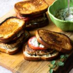 Greek Turkey Burgers on a cutting board with a green bowl of Tzaziki sauce.