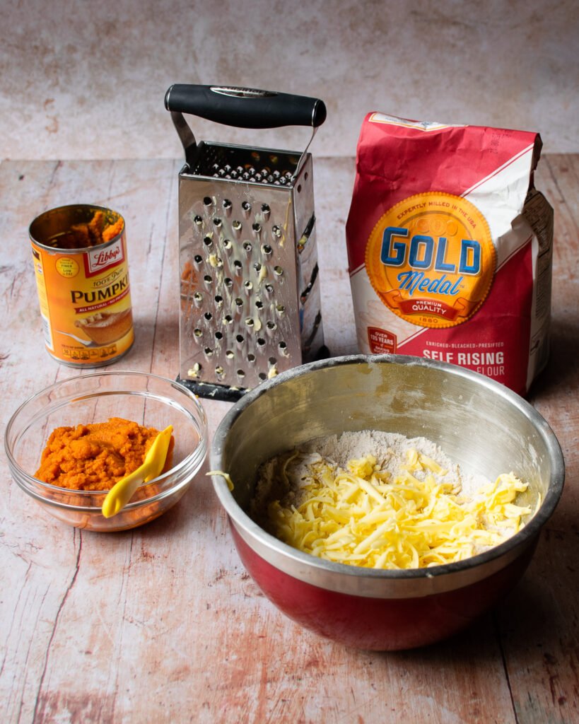 Ingredients on a table - flour, butter, pumkin purée and a grater.
