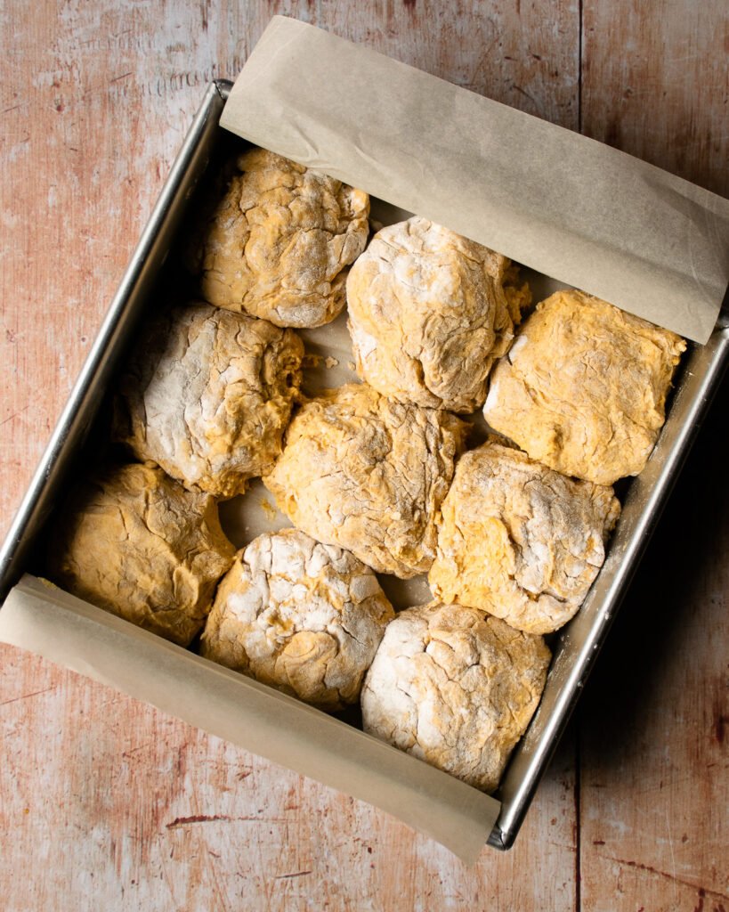 Nine pumpkin buttermilk biscuits in a square cake pan lined with parchment paper.
