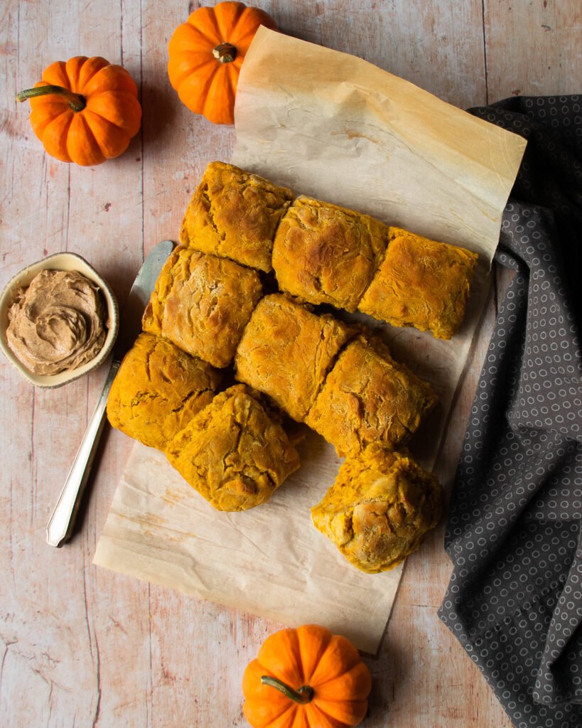 Pumpkin biscuits turned out of the cake pan and on a piece of parchment paper with cinnamon sage butter and a knife.