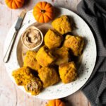 Pumpkin buttermilk biscuits on a white platter with mini pumpkins and cinnamon sage butter.