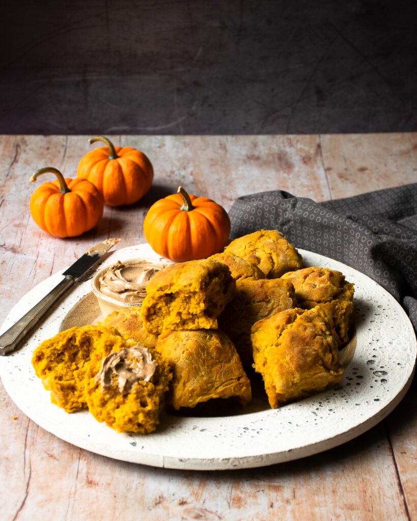 A white platter of pumpkin biscuits with mini pumpkins in the background.