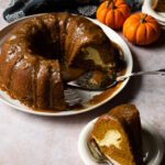 Pumpkin Cream Cheese Bundt Cake on a platter with a piece on a plate in the foreground.