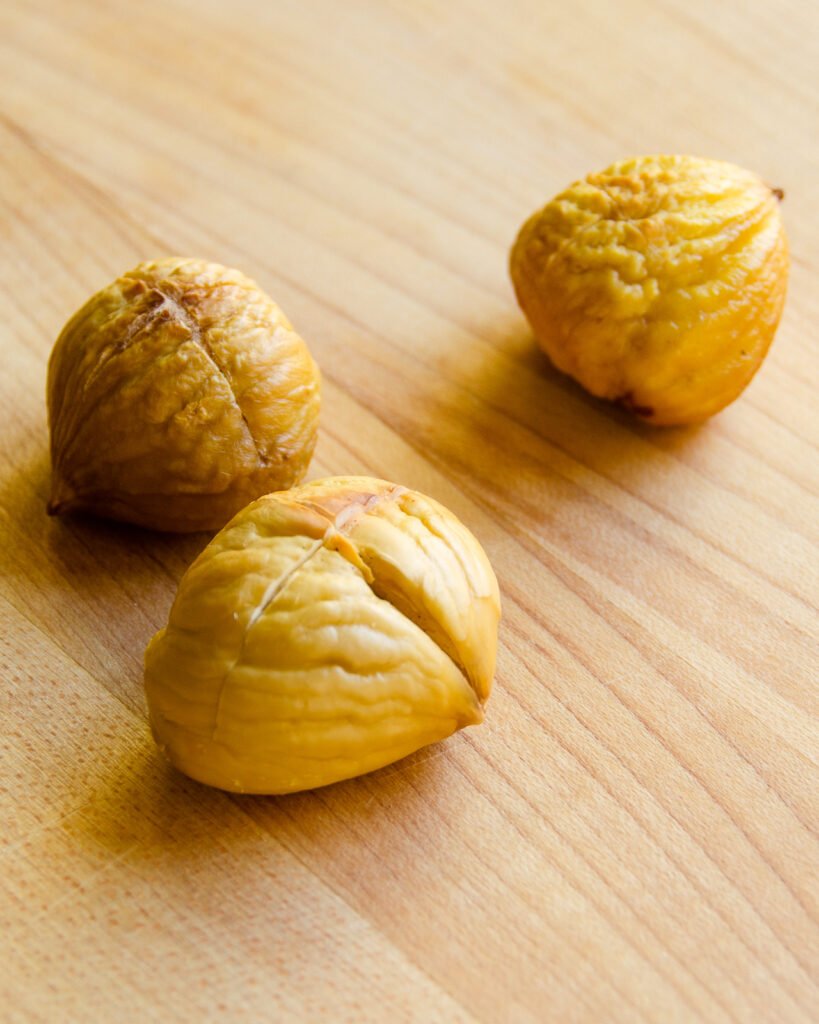 Three shelled and peeled chestnuts on a cutting board.