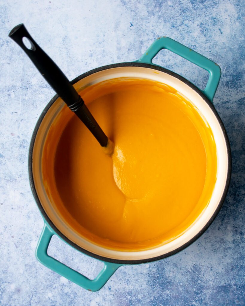 Carrot Ginger Orange Soup puréed in a Dutch oven with a ladle sticking out of it.