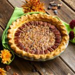 Chocolate Bourbon Pecan Pie on a wooden table with flowers and a green napkin.