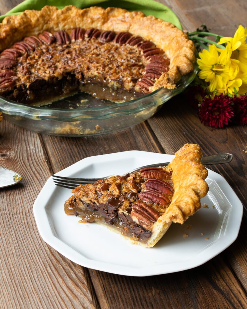 A piece of pie in front of the whole pie on a wooden table.