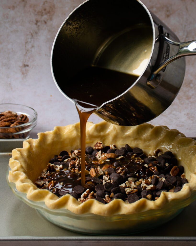 Pouring the sugar filling into chocolate bourbon pecan pie.