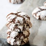 Four chocolate crinkle cookies stacked on each other with other cookies in the background.